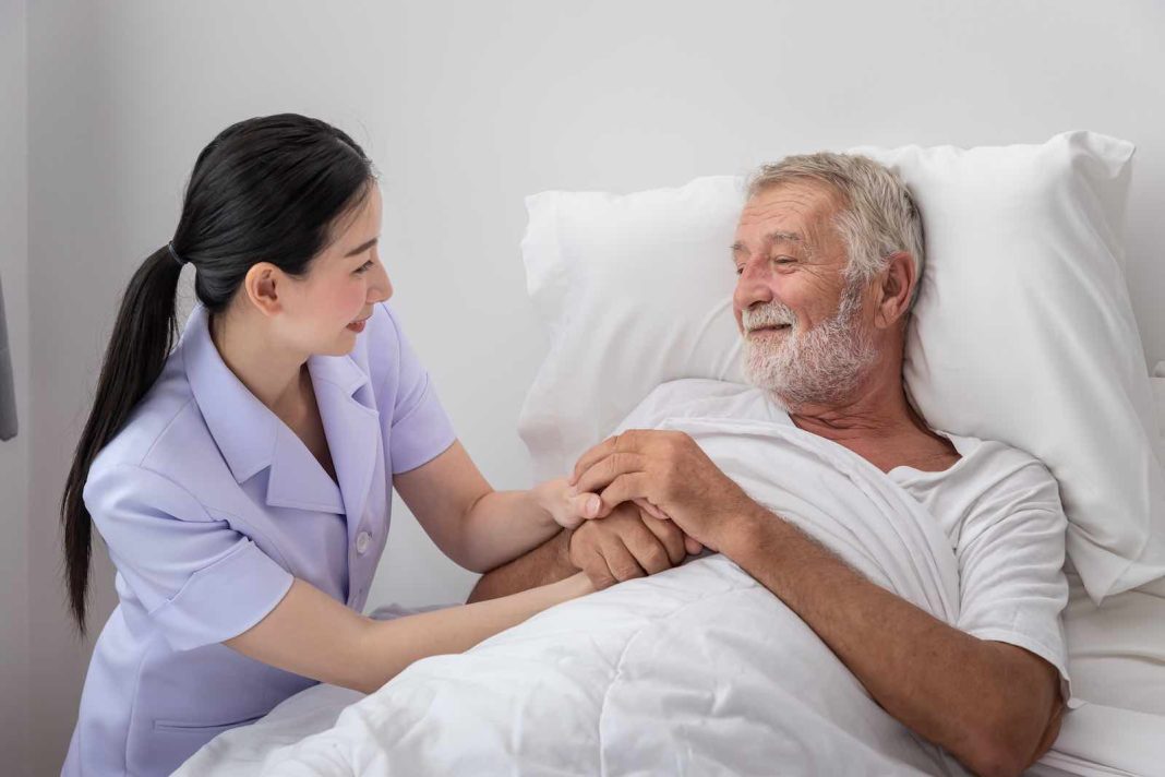 Happy nurse holding elderly man hands with blanket in bedroom at nursing home Planning for an Aging Parent